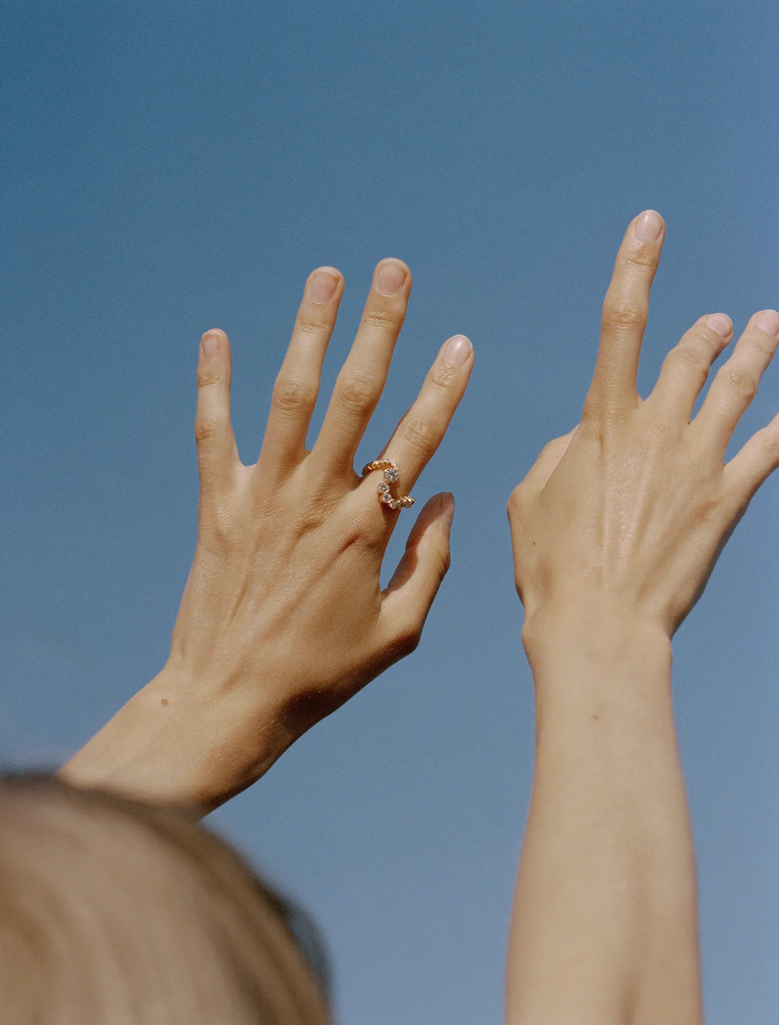 Hands pointing towards the sky, left index finger is wearing Grand Ensemble Ocean ring 