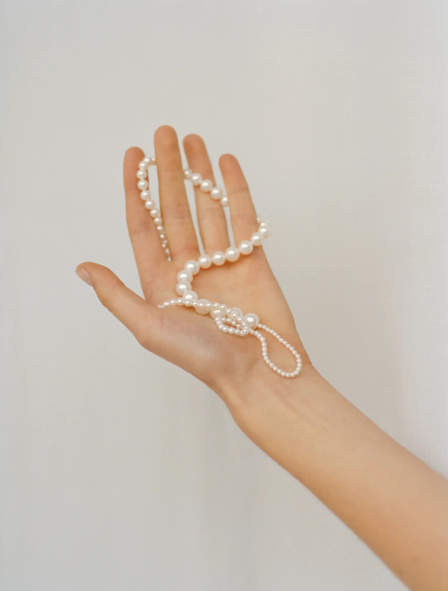 Showing palm of model's hands holding Peggy pearl necklace  