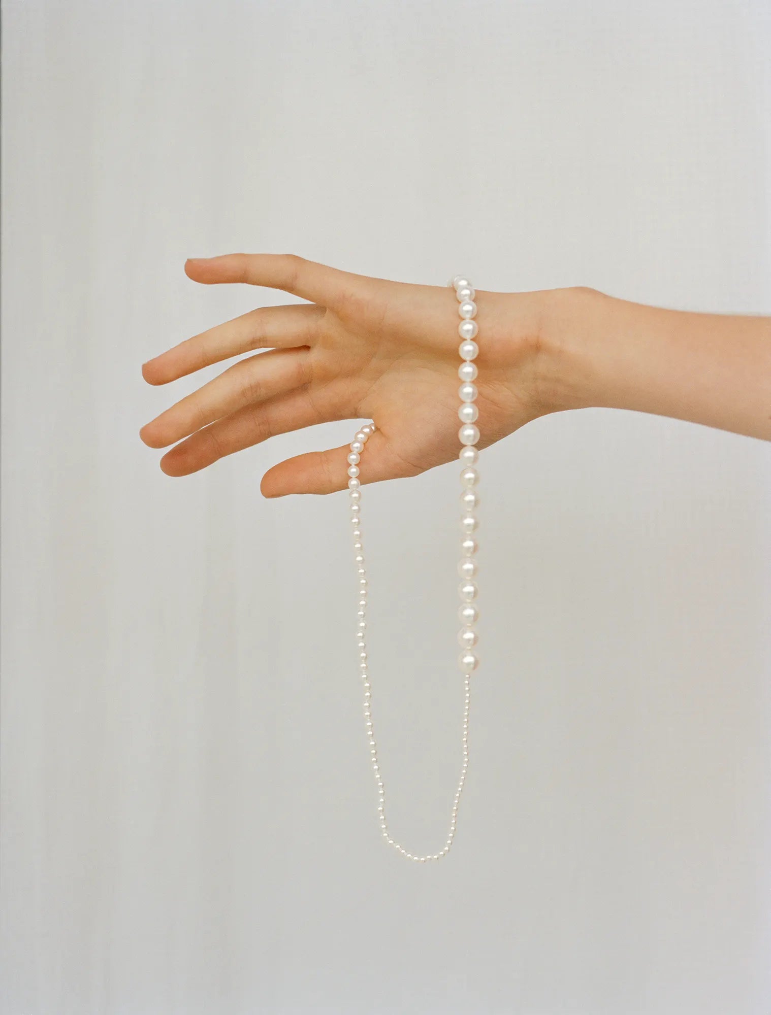 Hand holding Peggy pearl necklace in front of grey background