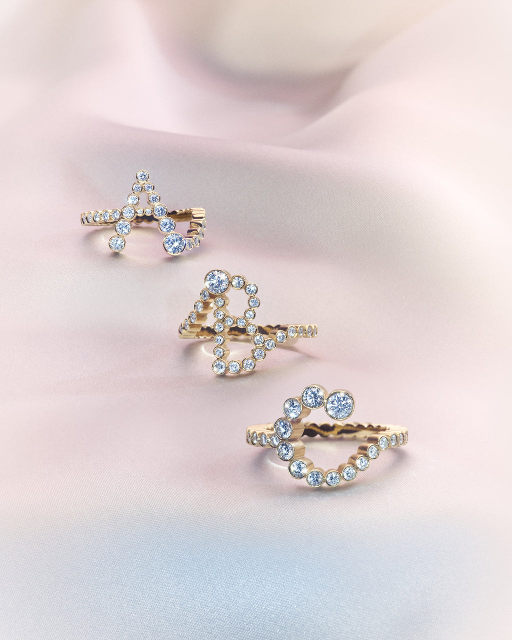 Three 18K yellow gold diamond rings shaped in the letters 'A', 'B' and 'C' on a soft pink background