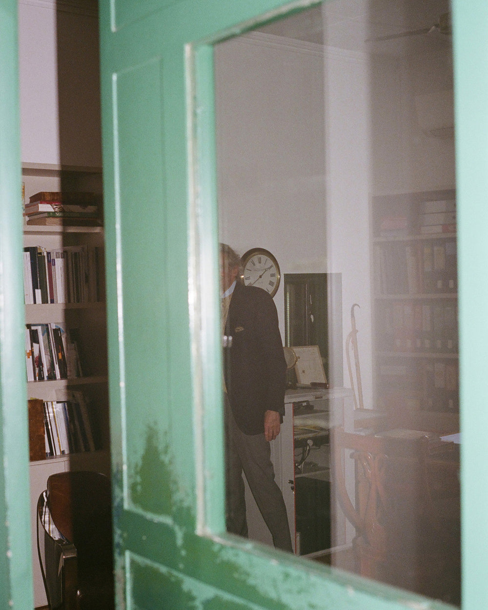 Person standing in a room with a green door and books on shelves.