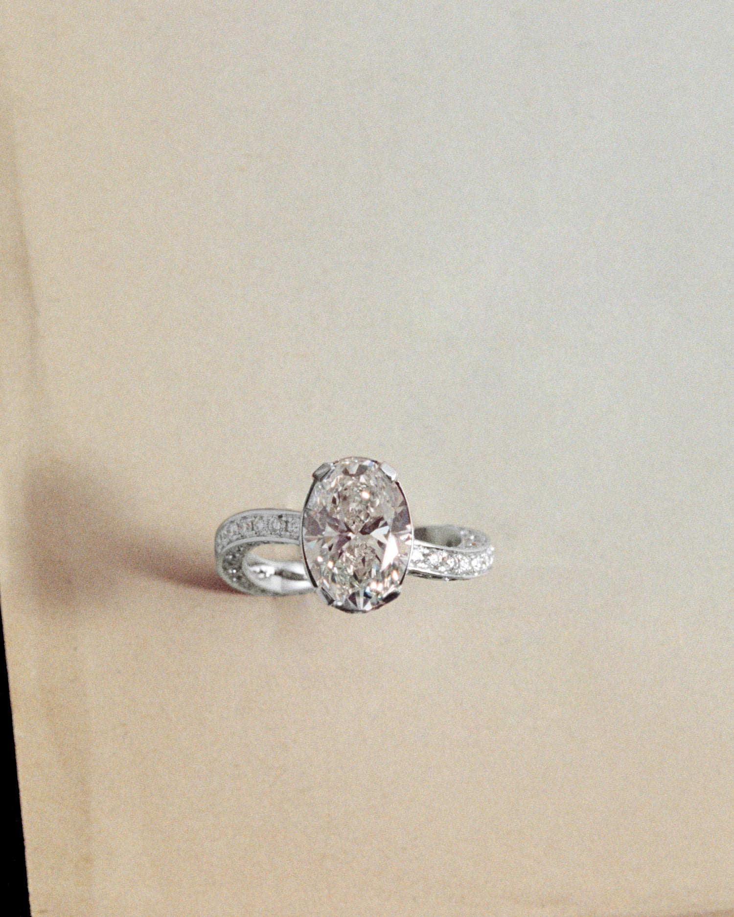 A ring in white gold with a large oval cut diamond at its center dancing on a light yellow background.