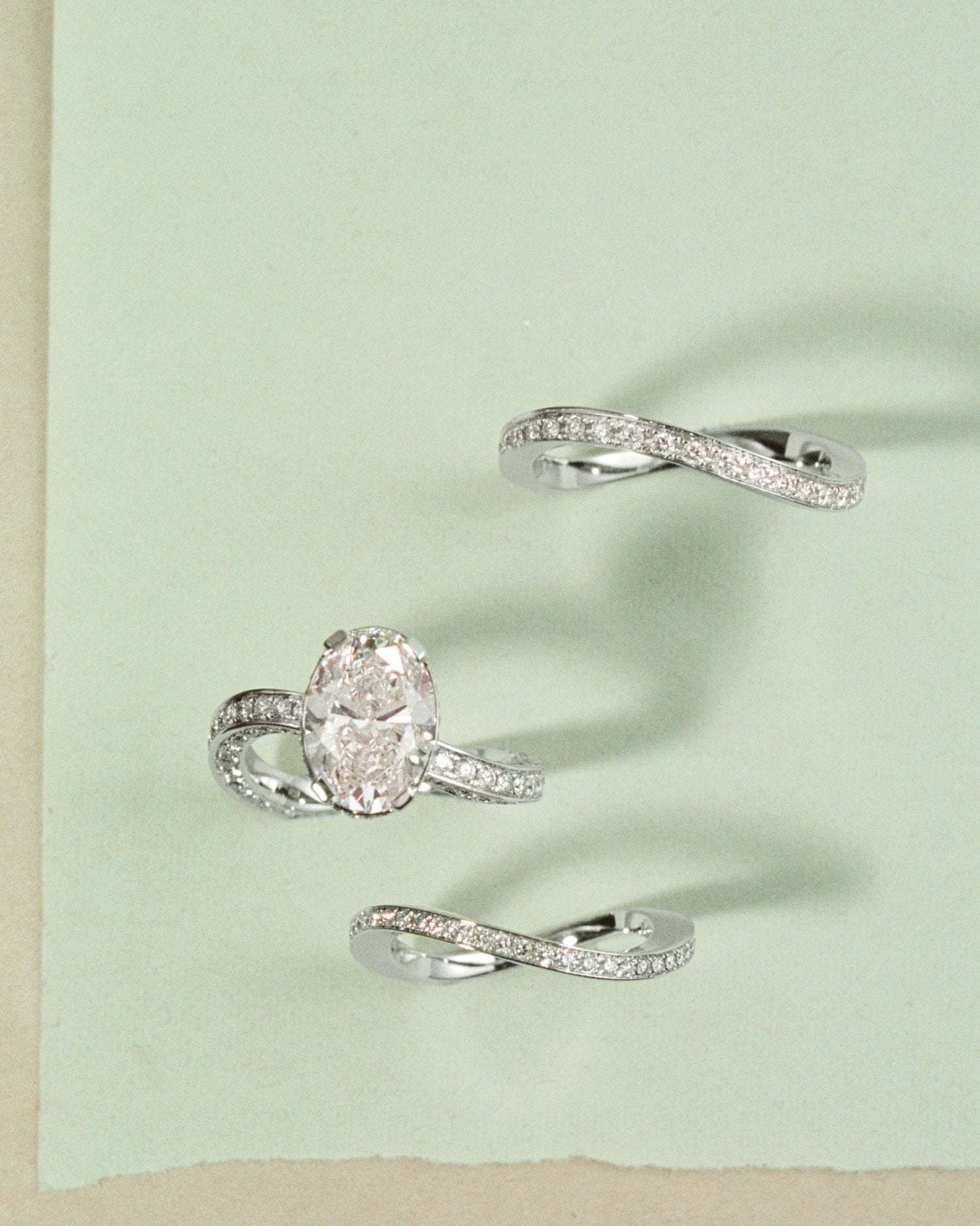 Set of three white gold rings with diamonds dancing on a light green background.